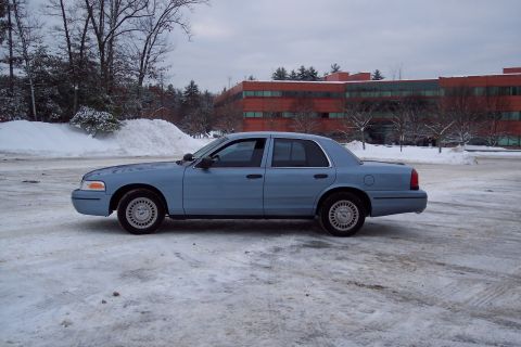 2001 Ford Crown Victoria - A blue 2001 Ford Crown Victoria is parked on a snowy surface with a modern building in the background.