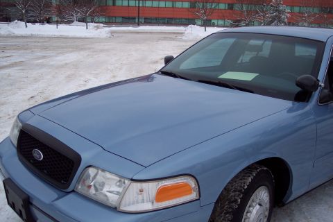2001 Ford Crown Victoria - A blue 2001 Ford Crown Victoria is parked on a snowy lot in front of a modern building.