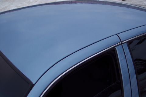 2001 Ford Crown Victoria - The roof and window of a blue sedan are visible in this close-up shot.