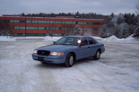 2001 Ford Crown Victoria - A blue 2001 Ford Crown Victoria is parked in a snowy lot with a large brick building in the background.