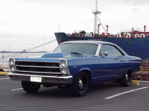 1966 Ford Fairlane - A blue 1966 Ford Fairlane coupe, a prominent hood scoop, is parked in front of a large cargo ship.