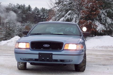 2001 Ford Crown Victoria - A light blue Ford Crown Victoria police car sits in a snowy landscape, with trees in the background.