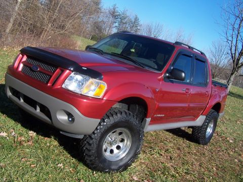 2002 Ford Sport Trac - This red 2002 Ford Sport Trac features a lifted suspension and aggressive off-road tires, giving it a stance on a grassy hillside.