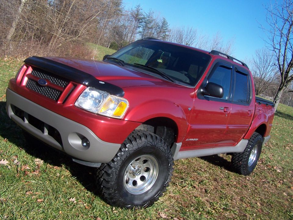 Red 2002 Ford Sport Trac with lifted suspension and off-road tires parked on grassy terrain