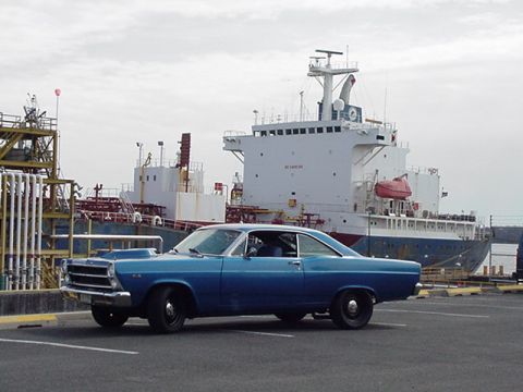 1966 Ford Fairlane - A blue 1966 Ford Fairlane is parked near a large cargo ship at a port.