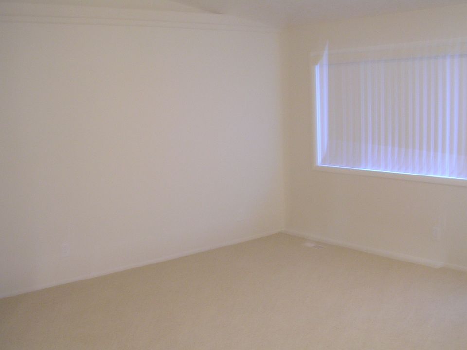 Interior of a room with beige carpet and walls, and a window with vertical blinds