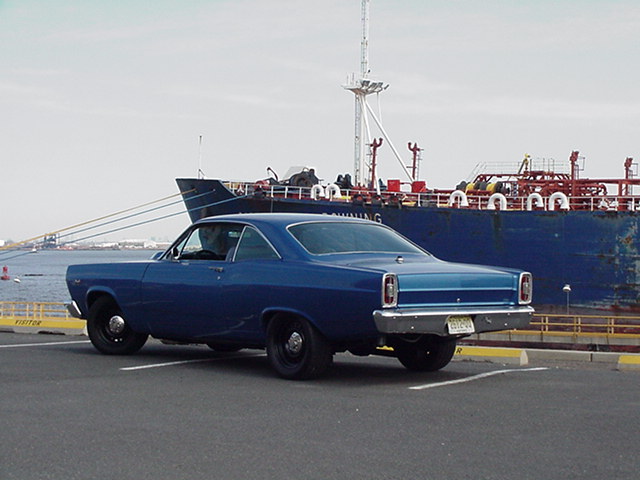 Blue 1966 Ford Fairlane coupe parked by a large ship