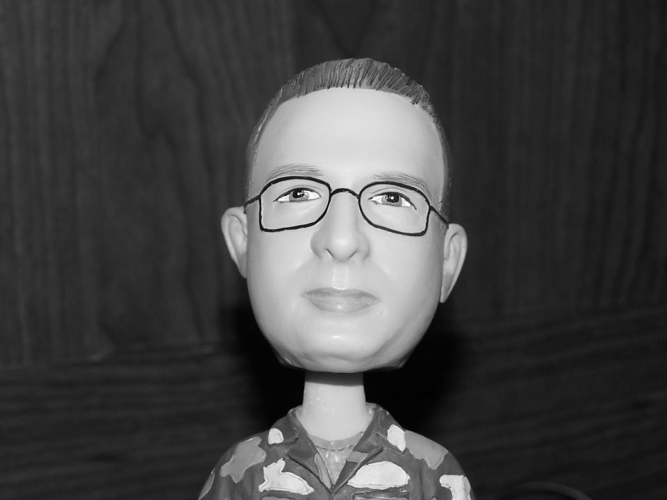 Black-and-white close-up of a bobblehead figurine in glasses and camo shirt