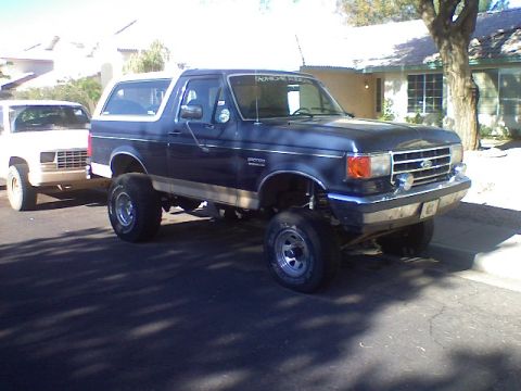1991 Ford Bronco - Lifted 1991 Ford Bronco parked on a residential street next to a white pickup truck.