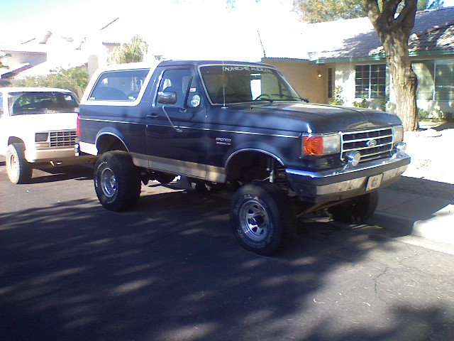 1991 Ford Bronco, lifted, parked next to a white pickup truck