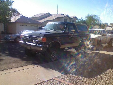 1991 Ford Bronco - A dark-colored Ford Bronco is parked in a residential driveway with a pickup truck behind it.