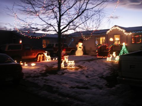 1995 Ford Bronco - A snowy yard is illuminated by festive Christmas lights and decorations on a house and trees.