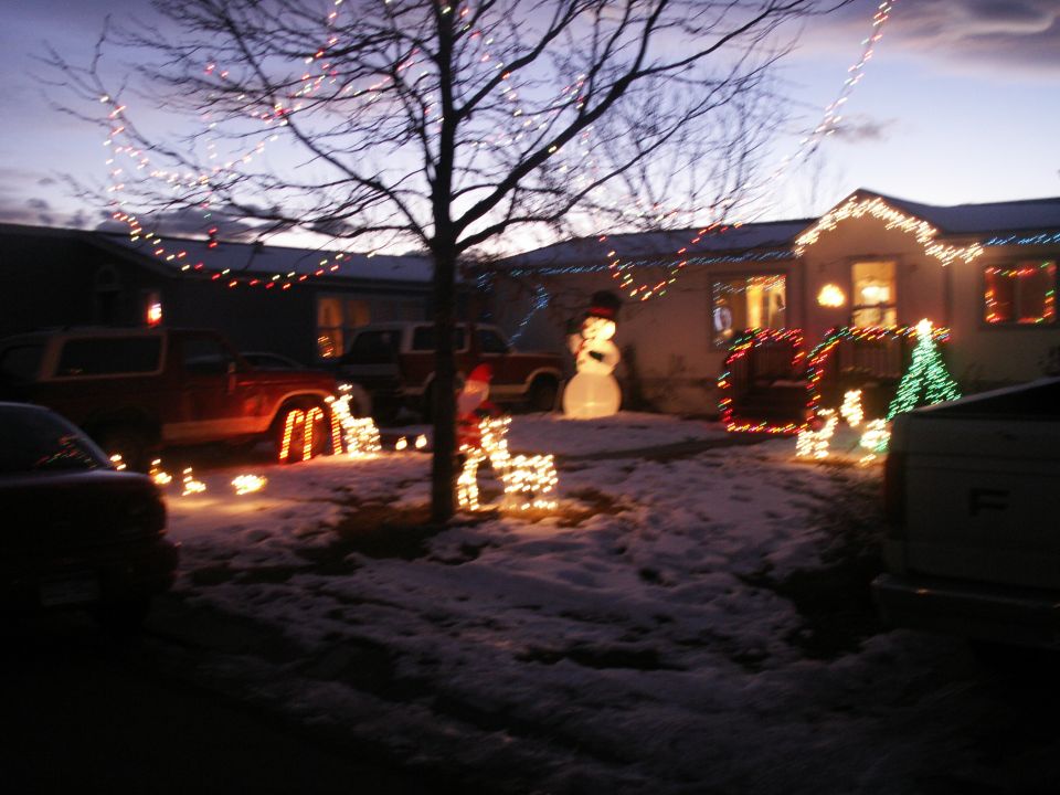 House decorated for Christmas with lights, snowman, and reindeer inflatables. Two trucks are parked in the driveway