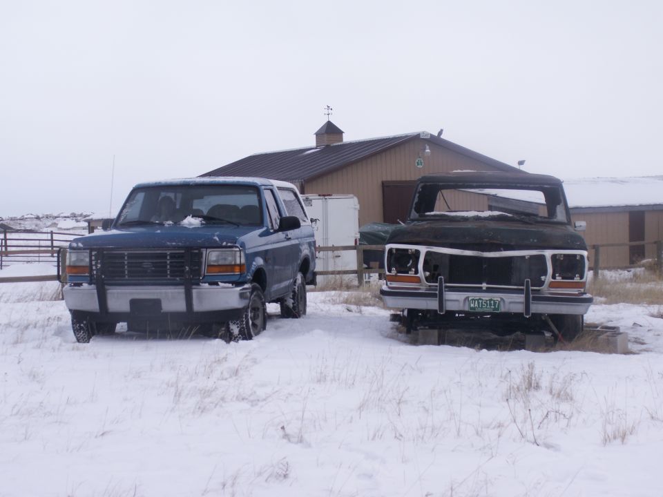 Blue 1992 Ford Bronco and a dark, damaged truck in a snowy field