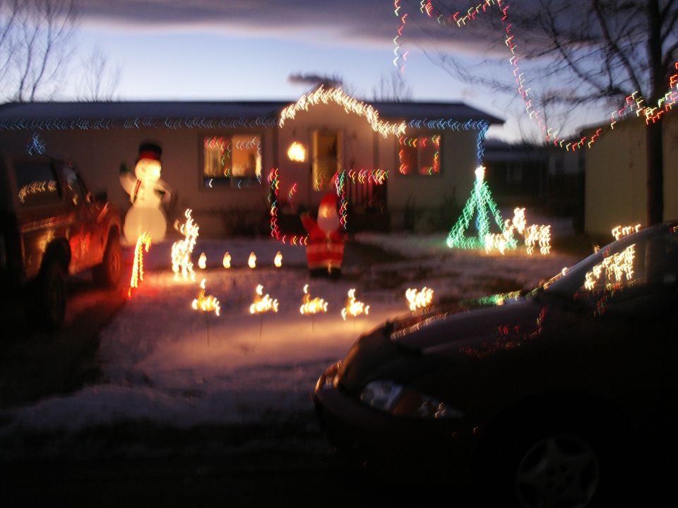 Two vehicles parked in front of a house decorated for Christmas with inflatable figures and lights