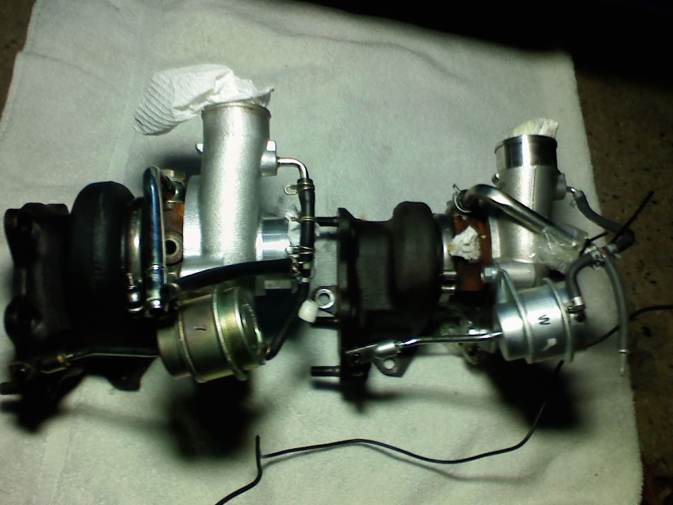 Two turbochargers with wastegate actuators on a white towel, inlets plugged with paper towel