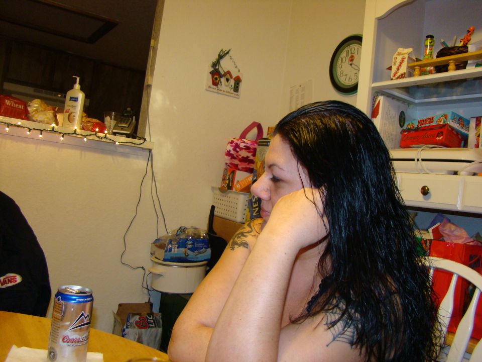 Woman with long dark hair and tattoos sits with arms crossed at a table with a can of Coors Light