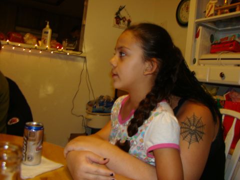 1989 Ford Bronco - A girl with a spider web tattoo on her arm is seated at a table, looking to the side.