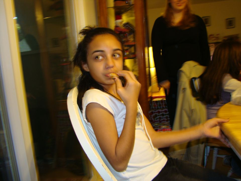 Girl eating a snack while sitting at a table, with other people in the background