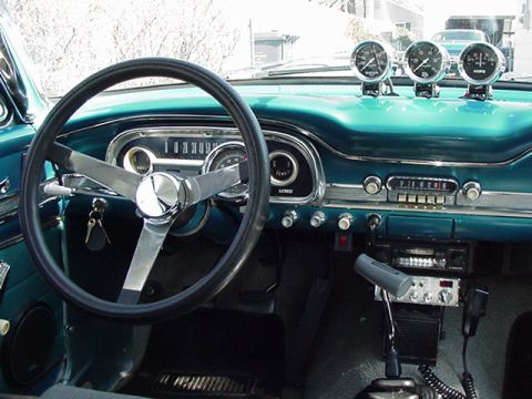 1966 Ford Fairlane - The dashboard of a classic car features a large steering wheel and three aftermarket gauges on top.