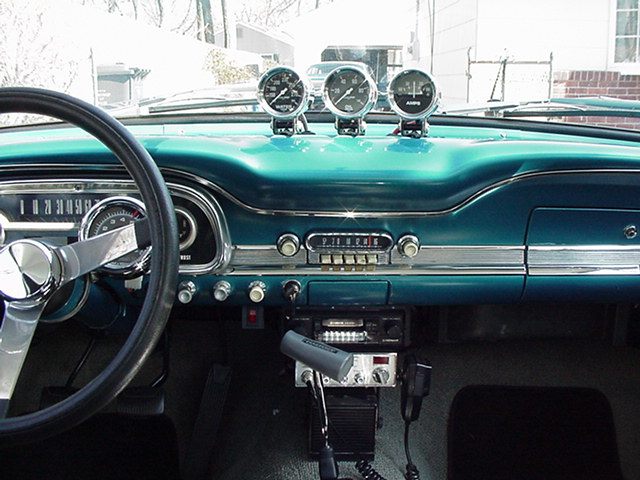 Dashboard of a classic car with a steering wheel, radio, and three gauges on top
