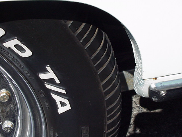 Radial T/A tire on chrome wheel under a white quarter panel with bare body filler at the arch