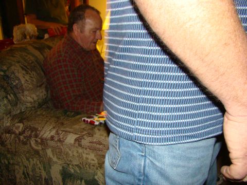 1989 Ford Bronco - A man in a red and black plaid shirt sits on a patterned couch, with another person's arm and torso in the foreground.