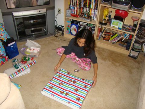 1989 Ford Bronco - A young girl is focused on wrapping a gift on the floor, surrounded by wrapping supplies and a bookshelf.