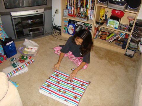 1989 Ford Bronco - A young girl sits on the carpet, focused on wrapping a gift with colorful striped paper.