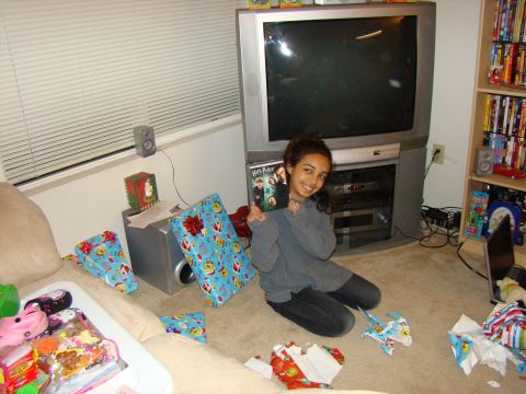 1989 Ford Bronco - A young woman sits on the floor surrounded by Christmas gifts and unwrapped presents, holding a DVD.