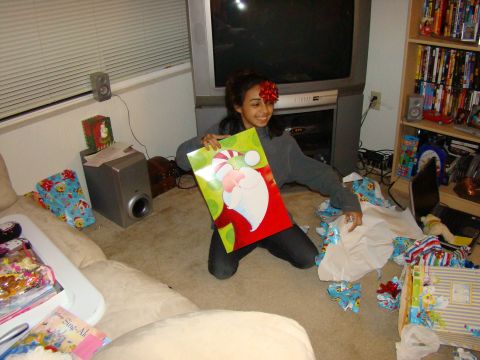 1989 Ford Bronco - A woman kneels on the floor, holding a Christmas gift bag, with presents and wrapping paper scattered around her.