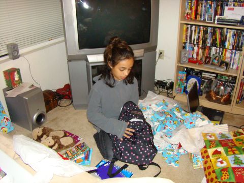 1989 Ford Bronco - A girl opens a backpack amidst wrapping paper and gifts in a room with a large television and bookshelf.