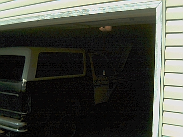 Dark garage view of a full-size Bronco SUV with white top, seen from the side through the open garage door