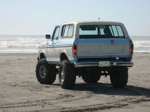 1978 Ford Bronco - This lifted 1978 Ford Bronco, seen from the rear, is parked on a sandy beach with the ocean in the background.
