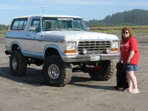 1978 Ford Bronco - A lifted 1978 Ford Bronco in two-tone blue and white is parked on a sandy beach with a woman and her dog nearby.
