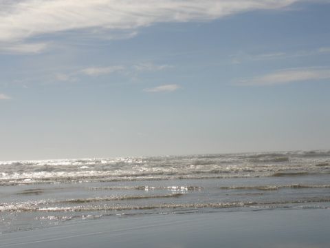 1978 Ford Bronco - A tranquil beach scene with gentle waves rolling onto the shore under a hazy sky, the Supermotors logo.