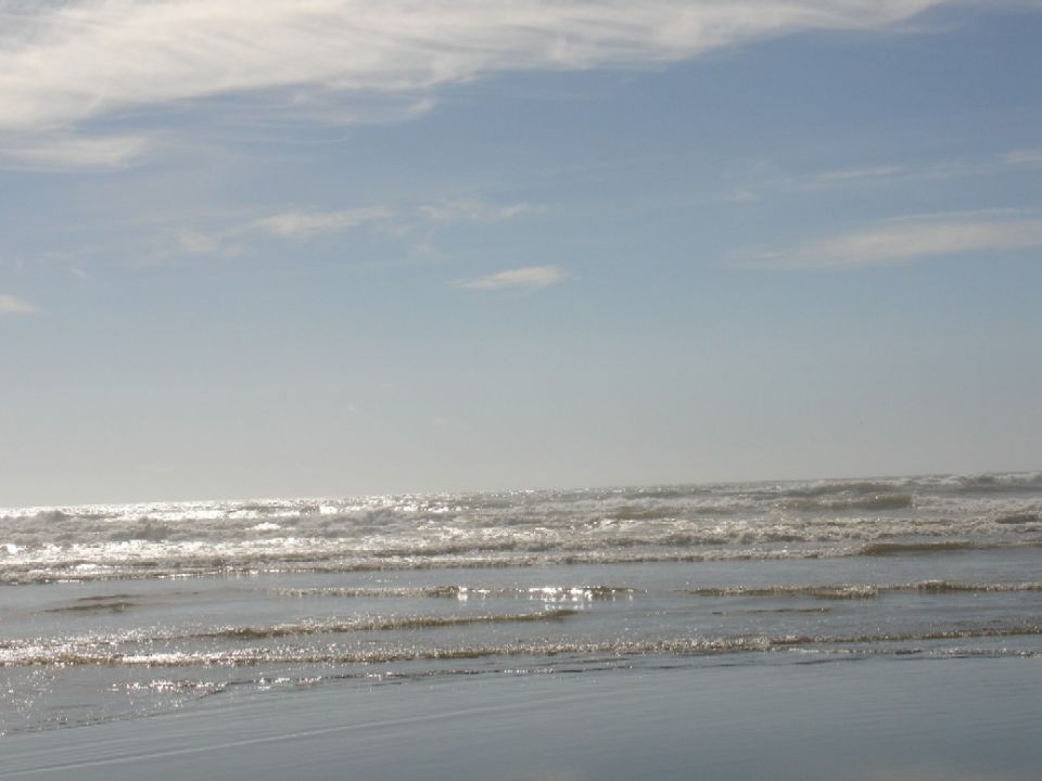 Ocean waves on a sandy beach under a cloudy sky. Supermotors logo in corner