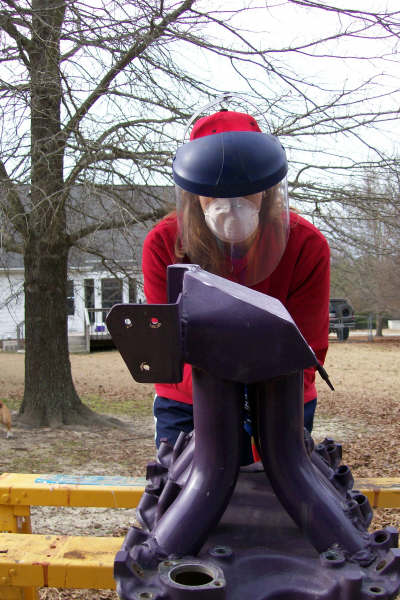 1988 Ford Bronco - A purple intake manifold is displayed on yellow sawhorses, with a person in protective gear behind it.