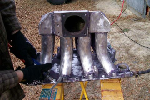 1988 Ford Bronco - A person in gloves works on a custom intake manifold, which is mounted on sawhorses outdoors.