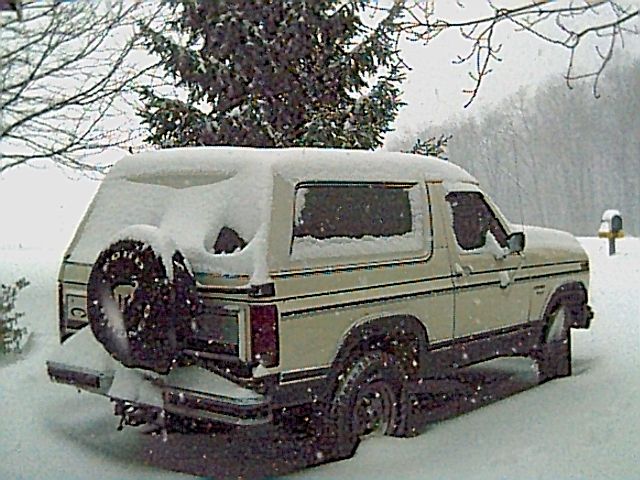 Tan 1987 Ford Bronco covered in snow, with a spare tire on the rear door