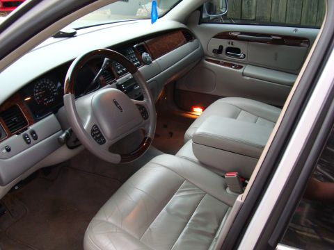 2002 Lincoln Town Car - The interior of a 2002 Lincoln Town Car features light gray leather seats and wood trim accents on the dashboard and steering wheel.