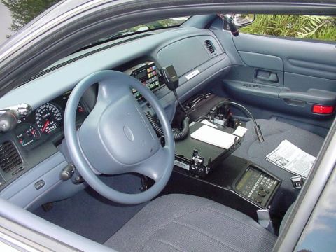 2001 Ford Crown Victoria - The interior of a 2001 Ford Crown Victoria police car is visible from the passenger side, highlighting the driver's area and police equipme…