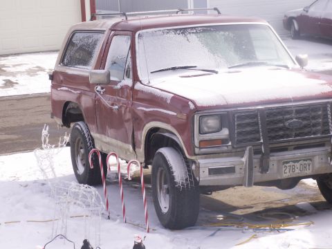 1986 Ford Bronco - A red SUV sits in the snow, adorned with holiday decorations like candy canes and a reindeer.