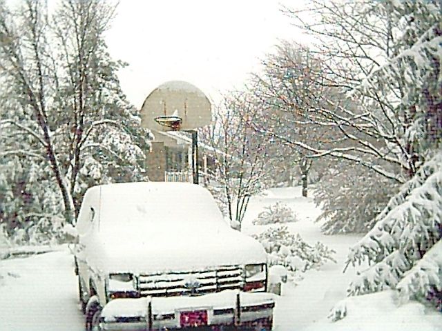 Snow-covered white Ford Bronco parked in a driveway during a snowstorm, front view
