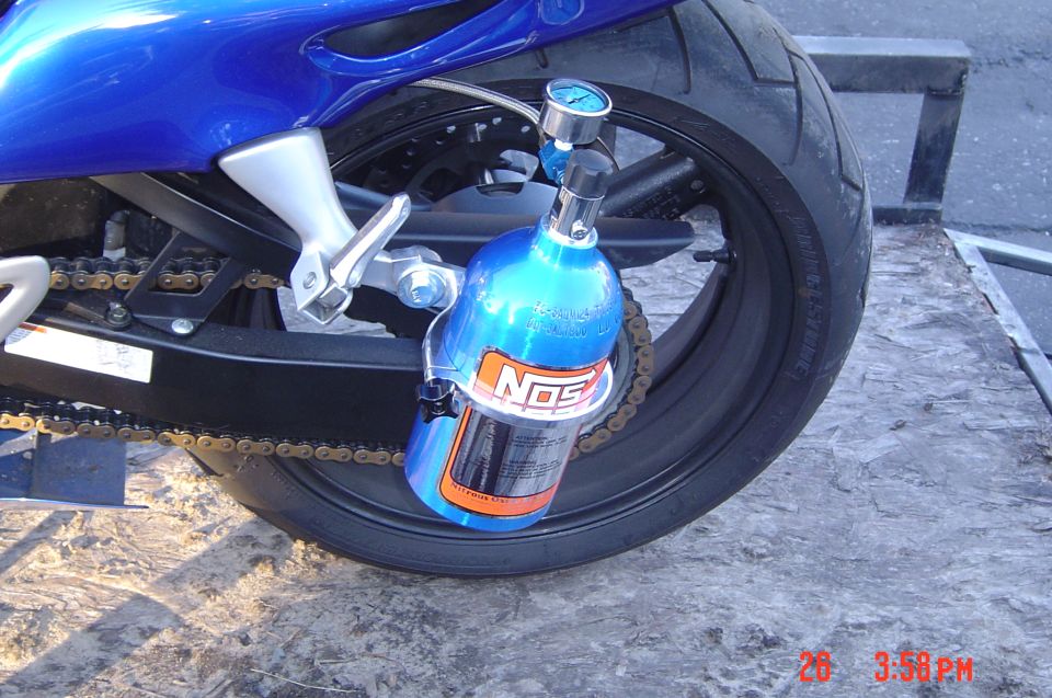 Blue motorcycle rear wheel with NOS bottle attached to the swingarm. Gold chain visible