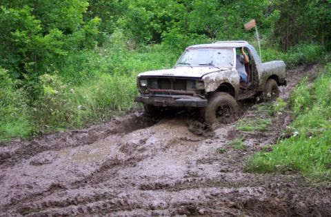 1995 Ford Bronco - A white pickup truck struggles to navigate a muddy off-road trail, with its front tires deeply embedded in the mire.