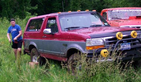1995 Ford Bronco - A red and grey 1995 Ford Bronco sits in tall grass, with another red truck visible behind it.