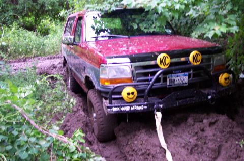 1995 Ford Bronco - This SUV is stuck in the mud, with off-road lights and decals visible on the front bumper.