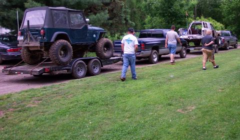 1995 Ford Bronco - A green Jeep Wrangler is loaded onto a trailer, towed by a Dodge Ram pickup truck, with other vehicles lined up behind.