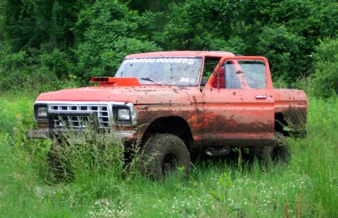 1995 Ford Bronco - This modified pickup truck is covered in mud and parked in a grassy field.